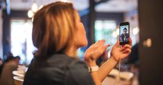 a woman holding up her cell phone to take a selfie with another person in the background