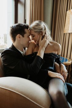 a man and woman sitting on top of a couch next to each other in front of a window