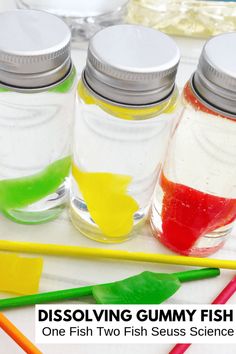 four glass jars filled with different colored liquids and paintbrushes on a table