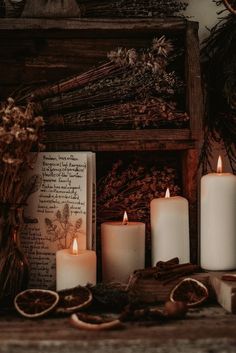 some candles are sitting on a table next to an open book and dried flowers in front of it