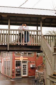 two people standing on top of a wooden balcony over looking the street and building below