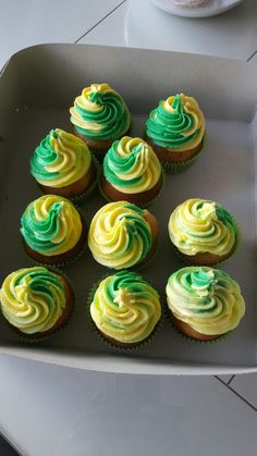 twelve cupcakes with green and yellow frosting in a box on a table