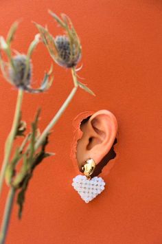 an ear with a heart shaped bead on it sitting next to a dried flower