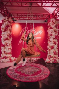 a woman sitting on a swing in the middle of a room with pink and white decorations