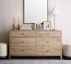 a wooden dresser sitting next to a white chair in a room with two pictures on the wall