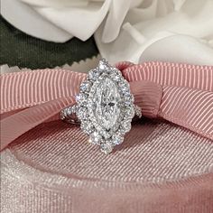 a diamond ring sitting on top of a pink ribbon next to a white rose flower