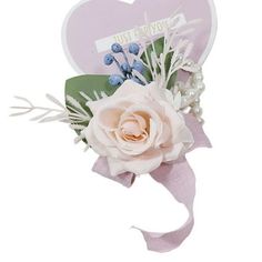 a white rose and some blue berries on top of a pink heart shaped brooch