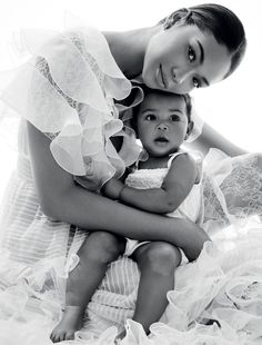 a woman holding a baby in her arms while posing for a black and white photo