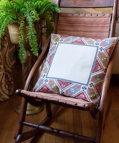 a wooden rocking chair with a pillow on top of it next to a potted plant