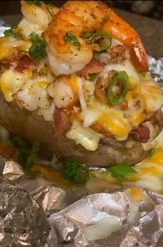 a baked potato covered in shrimp and cheese on tin foil with sauce drizzled over it