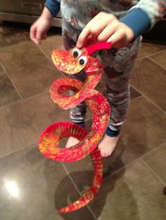 a young boy holding onto a red snake sculpture on top of a tile floor in front of an oven