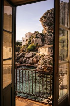 an open window looking out at the water and houses on top of a rocky hill