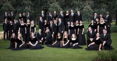 a group of people dressed in black posing for a photo together on the grass with trees in the background