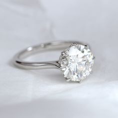 a diamond ring sitting on top of a white cloth covered tablecloth, with the center stone partially surrounded by two clawed prongs