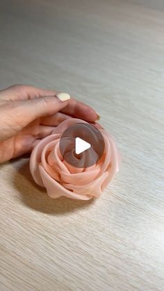 a woman's hand holding a pink flower on top of a wooden table