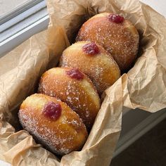 three doughnuts in a brown paper bag on a window sill, with powdered sugar sprinkled on top