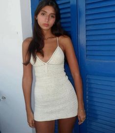 a woman standing in front of a blue door wearing a white crochet dress