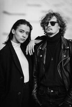 a man and woman standing next to each other wearing black leather jackets, white turtle neck sweaters