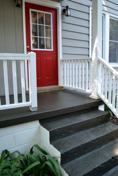 a red door is on the side of a gray house with white railings and steps