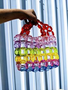 a hand holding a multicolored bag made out of glass beads and stringing