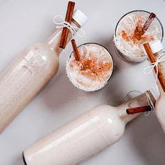 two glasses filled with drinks next to cinnamon sticks and an empty bottle on a table