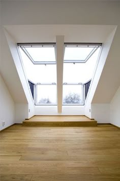 an empty room with two large windows in it's center and wooden flooring