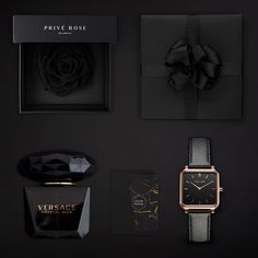 three watches, one watch and two perfumes on a black surface with roses in the background