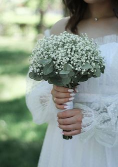 a woman in a white dress holding a bouquet of baby's breath and greenery