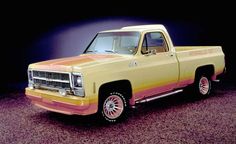 an old yellow truck with pink stripes on the front and back tires, parked in a dark room