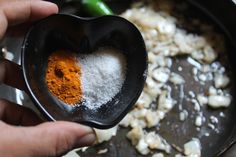 a person holding a spoon with some food in it on top of a pan filled with onions and spices