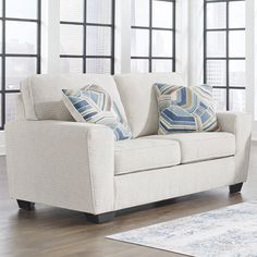 a white couch with two pillows on it in front of large windows and a rug