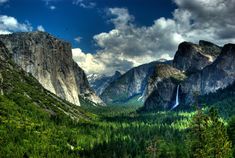 the valley is surrounded by tall mountains and green trees, with a waterfall in the middle