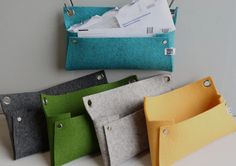 four different colored felt envelopes are lined up on a white table with pins in them