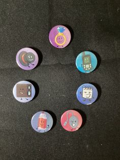 six buttons with different designs on them sitting on a black surface in the shape of a circle