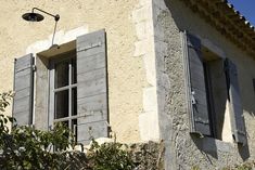 an old building with two windows and shutters on the outside, in front of a blue sky