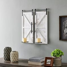 two white shutters are hanging on the wall above a table with candles and other items