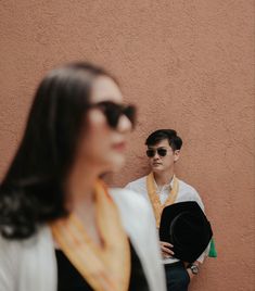 two people standing next to each other with sunglasses on and one person holding a hat