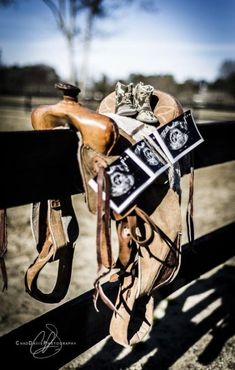 a horse saddle sitting on top of a wooden fence next to a cowgirl's boot