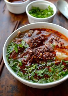 a bowl of soup with meat and vegetables in it on a wooden table next to spoons