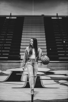 a woman holding a basketball while standing in front of some bleachers