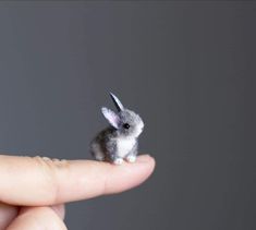 a tiny toy rabbit sitting on top of a persons finger in front of a gray background