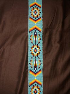 a blue and yellow beaded bracelet on a brown cloth with an orange, white, and green design