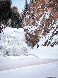 a man standing in front of a waterfall covered in snow next to trees and rocks