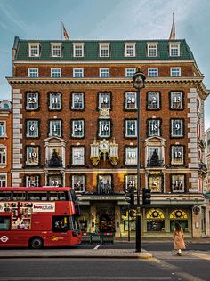 a red double decker bus parked in front of a tall brick building with many windows