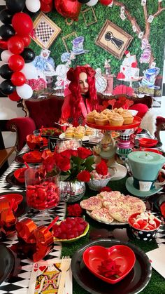 a table topped with lots of red and black plates covered in food next to balloons