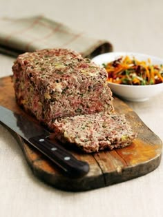 sliced meatloaf sitting on top of a cutting board next to a bowl of salad