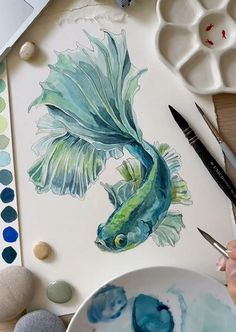 someone is painting a fish with watercolors on paper