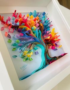 a colorful tree made out of folded paper in a white shadow box on a table