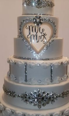 a three tiered wedding cake decorated with silver and white frosting, hearts and the words mr and mrs on top