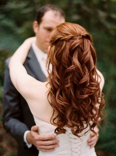 a bride and groom embracing each other in front of some trees with long red hair